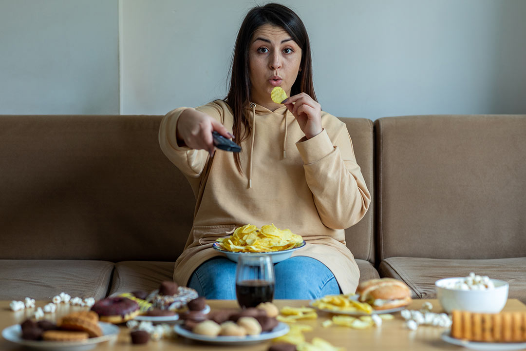 Overweight woman sit on the sofa with junk food